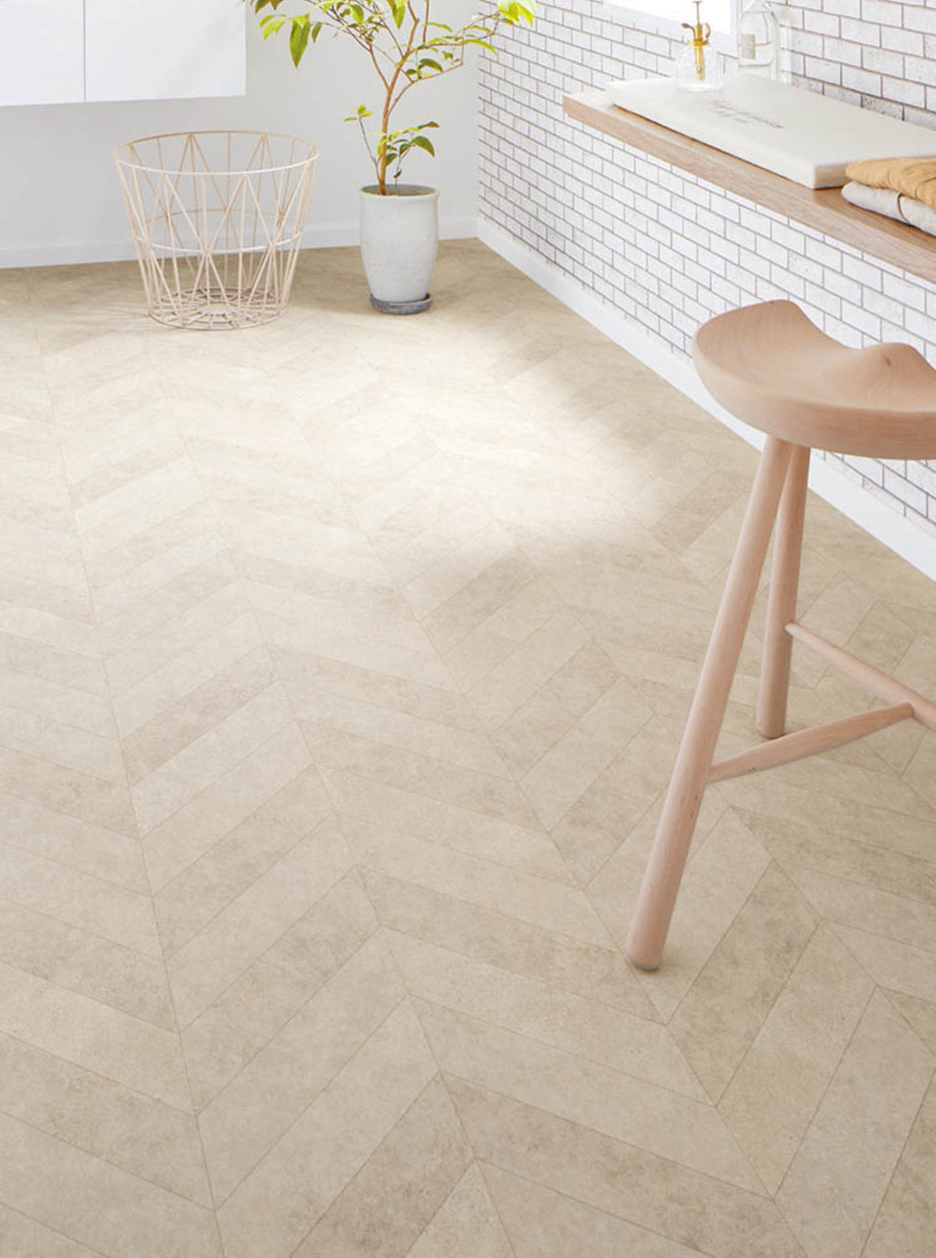 Beige herringbone patterned floor with a wooden stool and plant in the background
